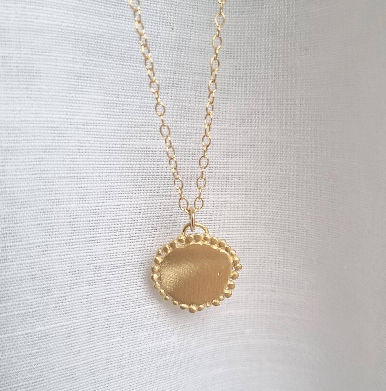 May include: A gold necklace with a round pendant that has a textured surface and a beaded edge.