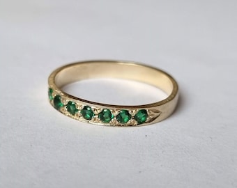 Puede incluir: Un anillo de banda de oro con una fila de piedras preciosas verde esmeralda.