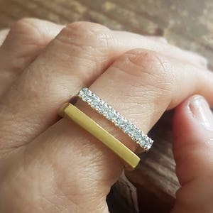 Może przedstawiać: Złoty pierścionek w kształcie pręta z rzędem małych diament&oacute;w osadzonych w cienkim pasku.