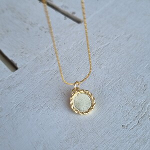 May include: A gold chain necklace with a round pendant. The pendant has a textured, rope-like design around the edge.