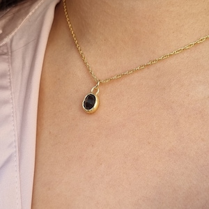 May include: A gold chain necklace with a small, oval-shaped pendant featuring a dark gemstone.