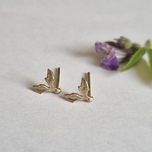 May include: A pair of gold-toned stud earrings shaped like small, textured leaves. Each earring features a delicate, organic silhouette with a post backing, designed to sit flush against the earlobe with a subtle, metallic sheen and detailed edges.