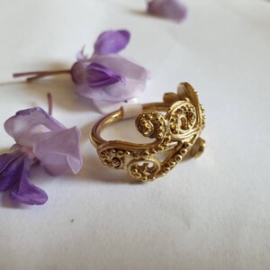 May include: A gold filigree ring with a delicate, intricate design. The ring is made of metal and has a smooth, polished finish.