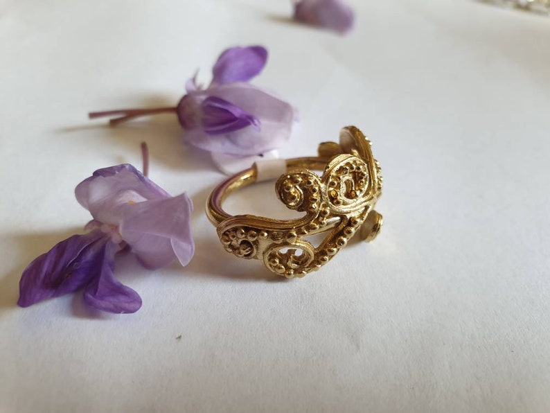 May include: A gold filigree ring with a delicate, intricate design. The ring is made of metal and has a smooth, polished finish.