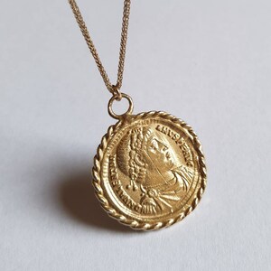May include: Gold chain necklace with a round pendant featuring a profile of a woman's face with a crown and the text "AUGUSTA" around the edge.
