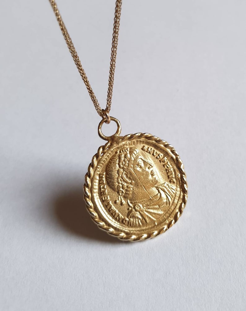 May include: Gold chain necklace with a round pendant featuring a profile of a woman's face with a crown and the text "AUGUSTA" around the edge.