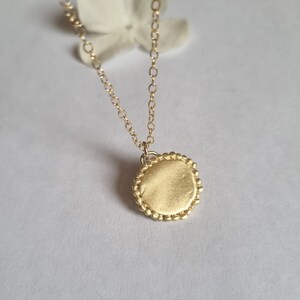May include: A gold necklace with a round pendant. The pendant has a textured surface and a beaded edge.
