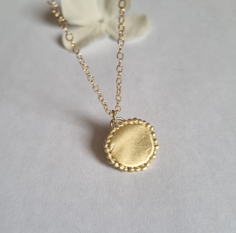 May include: A gold necklace with a round pendant. The pendant has a textured surface and a beaded edge.