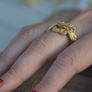 May include: A gold ring with a delicate, intricate design featuring a series of connected loops and small beads.