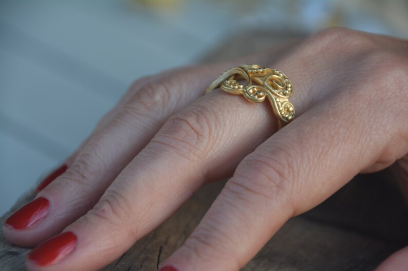May include: A gold ring with a delicate, intricate design featuring a series of connected loops and small beads.