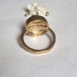 May include: A gold ring with a large, round, smooth, bezel-set stone. The ring is thick and has a textured band.