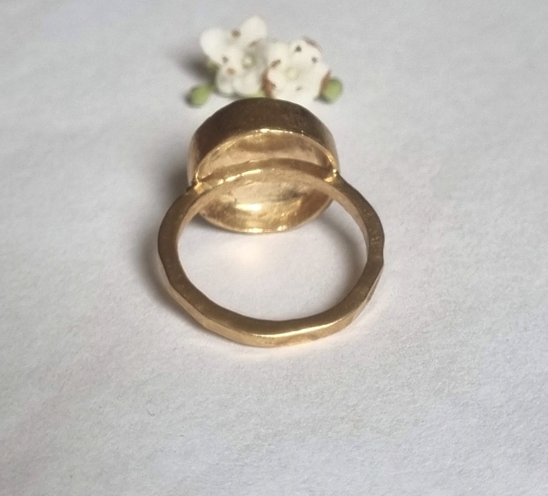 May include: A gold ring with a large, round, smooth, bezel-set stone. The ring is thick and has a textured band.
