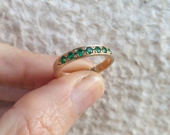May include: A gold band ring with a row of emerald green gemstones.