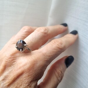 Op de afbeelding: Een zilveren ring met een grote, ronde, donkerbruine edelsteen.
