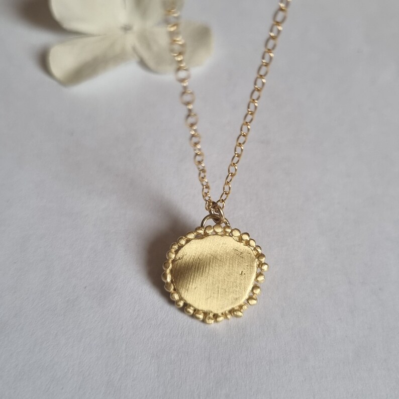 May include: A gold necklace with a round pendant. The pendant has a textured surface and a beaded edge.