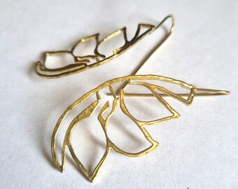 May include: A pair of gold-toned earrings with a delicate, abstract floral design. The earrings are made of thin metal and have a slightly textured finish.