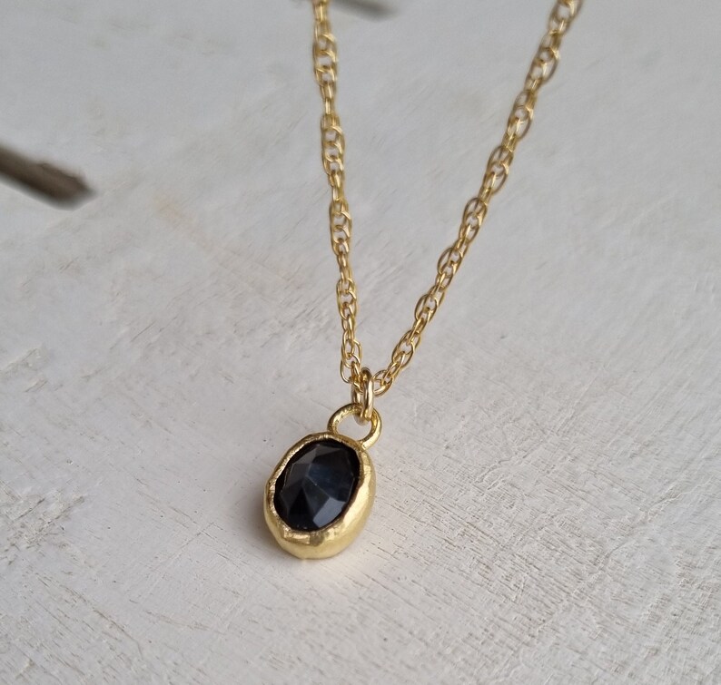 May include: A gold chain necklace with a black gemstone pendant. The pendant is oval shaped and has a faceted surface.