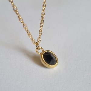 May include: A gold chain necklace with a black gemstone pendant. The pendant is oval shaped and has a textured gold setting.