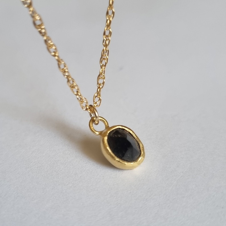 May include: A gold chain necklace with a black gemstone pendant. The pendant is oval shaped and has a textured gold setting.