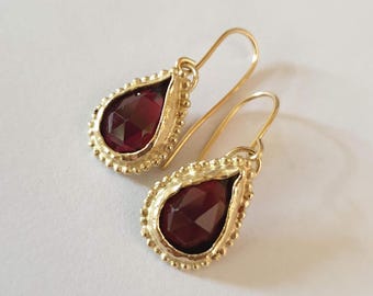 May include: A pair of gold teardrop earrings with red gemstone accents.