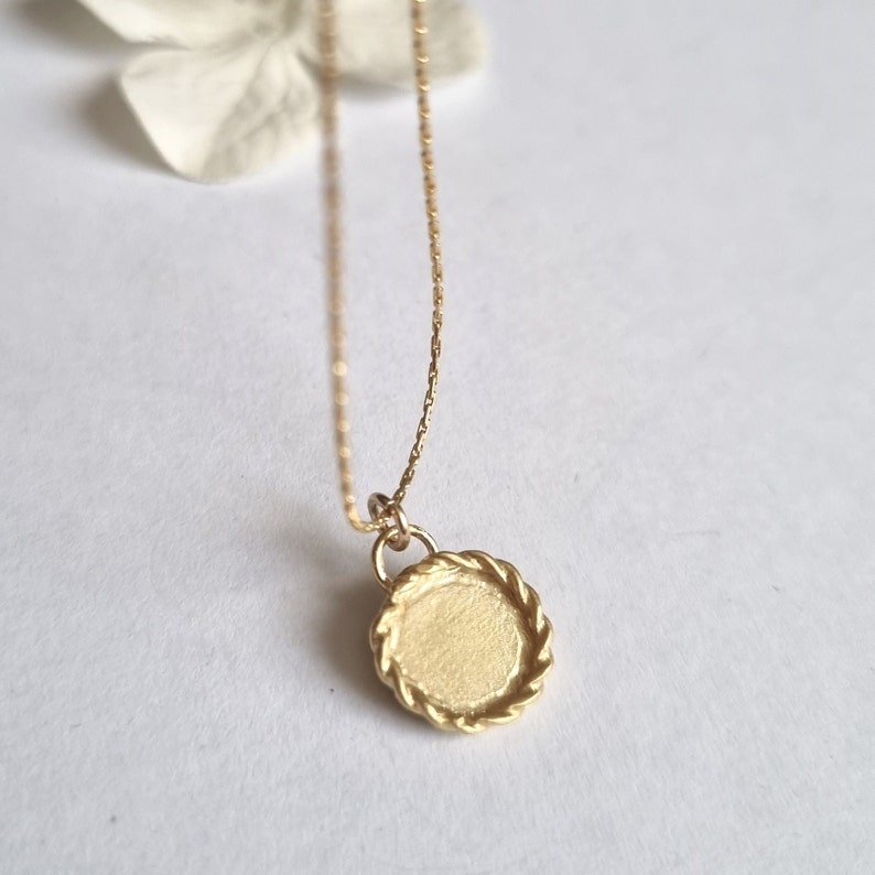 May include: A gold necklace with a round pendant featuring a textured, rope-like border.
