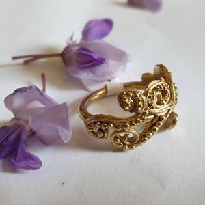 May include: A gold ring with a delicate, intricate design. The ring is made of a single piece of metal and has a floral pattern.