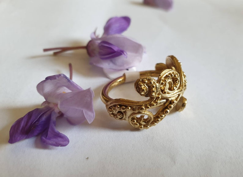 May include: A gold ring with a delicate, intricate design. The ring is made of a single piece of metal and has a floral pattern.