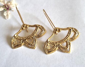 May include: A pair of gold-tone earrings with a delicate, intricate design. The earrings are shaped like a stylized flower with multiple layers of petals.