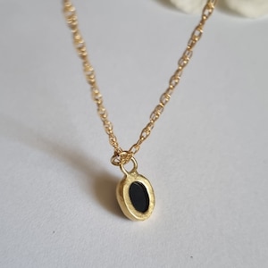 May include: A gold chain necklace with a small oval pendant featuring a black stone.