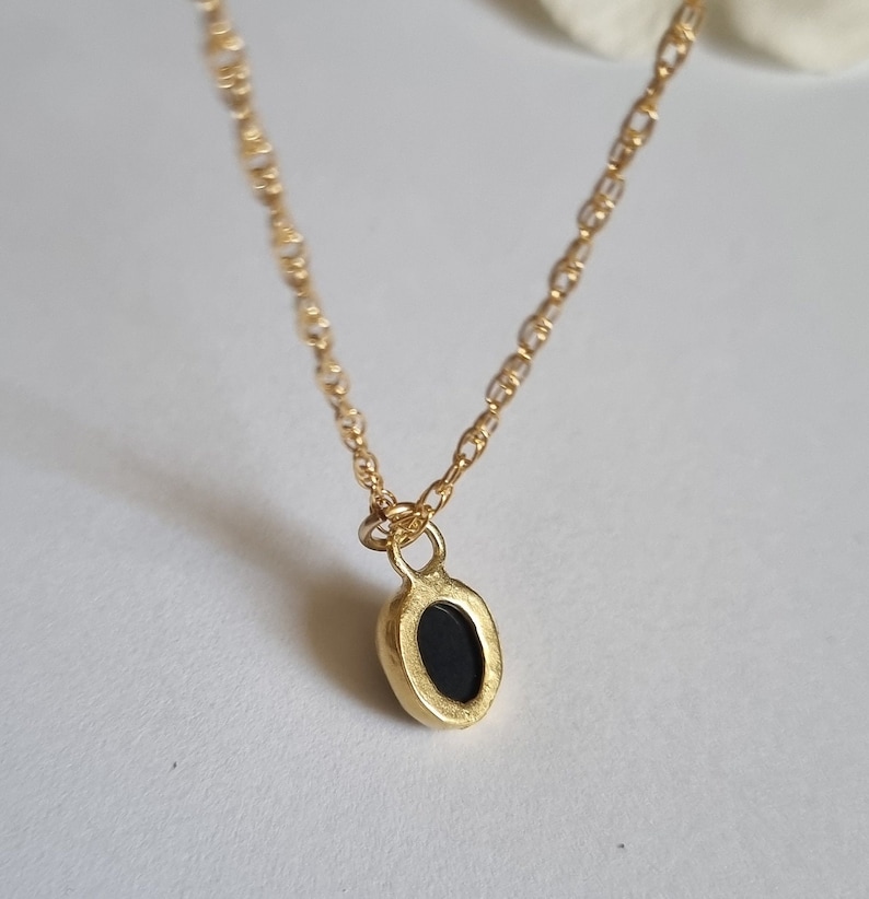 May include: A gold chain necklace with a small oval pendant featuring a black stone.