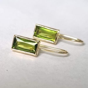 May include: A pair of gold earrings with green rectangular gemstones. The earrings have a simple, minimalist design.
