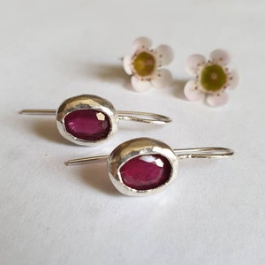 May include: A pair of silver earrings with a pink gemstone set in each. The earrings have a hammered texture and a simple hook closure.