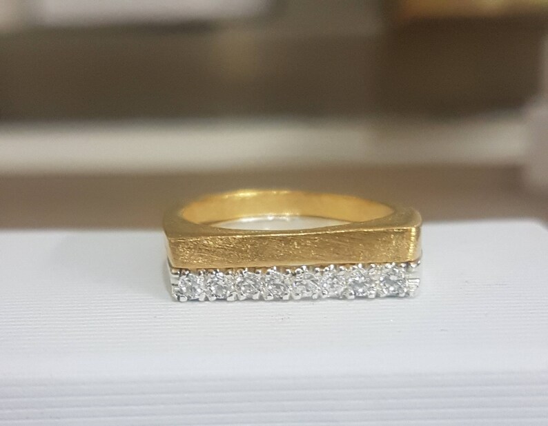 Może przedstawiać: Złoty pierścionek z kwadratową obrączką i rzędem małych diament&oacute;w.