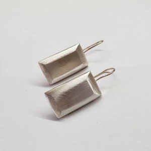 May include: A pair of silver earrings with a rectangular shape and a brushed finish. The earrings have a simple, modern design.