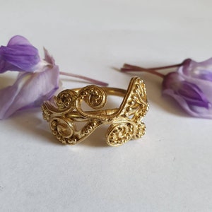May include: A gold ring with a delicate, intricate design featuring swirling patterns and small beads. The ring is made of metal and has a unique, handcrafted look.