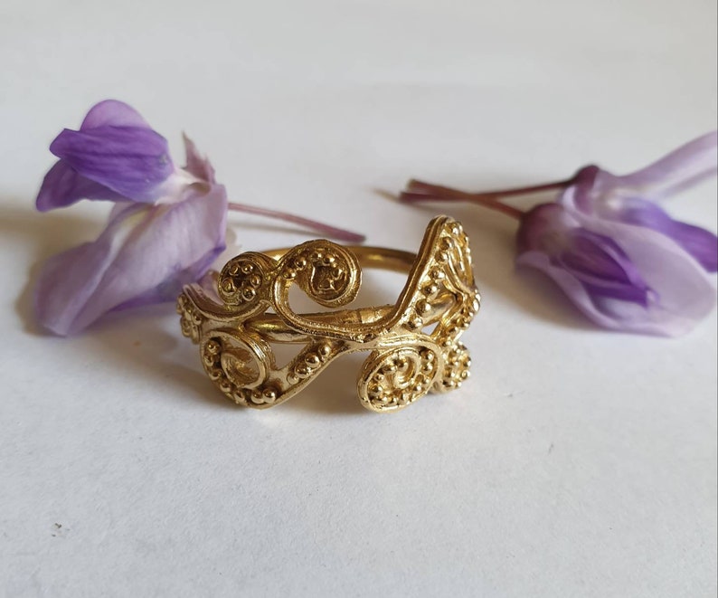 May include: A gold ring with a delicate, intricate design featuring swirling patterns and small beads. The ring is made of metal and has a unique, handcrafted look.