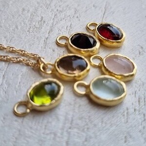 May include: A set of seven gold-toned oval pendants with different colored gemstones. The pendants have a textured edge and a small loop at the top for attaching to a chain.