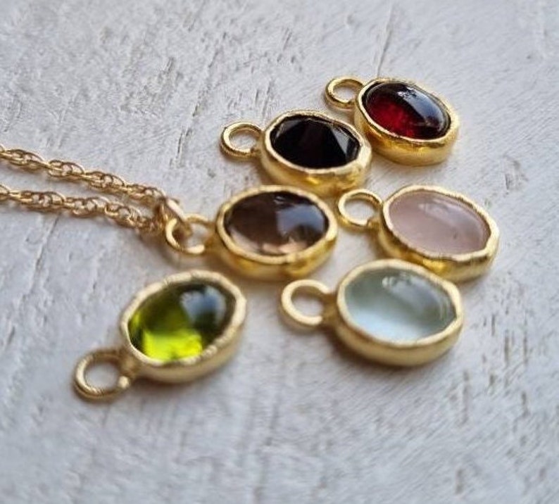 May include: A set of seven gold-toned oval pendants with different colored gemstones. The pendants have a textured edge and a small loop at the top for attaching to a chain.