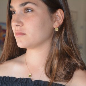 May include: A woman wearing a gold necklace and earrings with a round pendant and matching earrings. The necklace and earrings are simple and elegant.