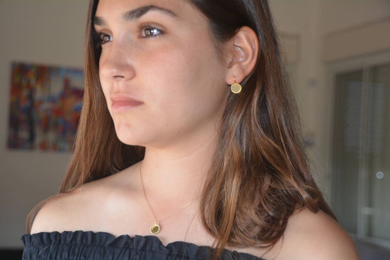 May include: A woman wearing a gold necklace and earrings with a round pendant and matching earrings. The necklace and earrings are simple and elegant.