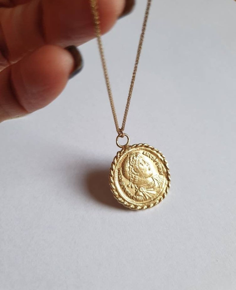 May include: A gold chain necklace with a round pendant featuring a profile of a woman's face. The pendant has a rope-like border.