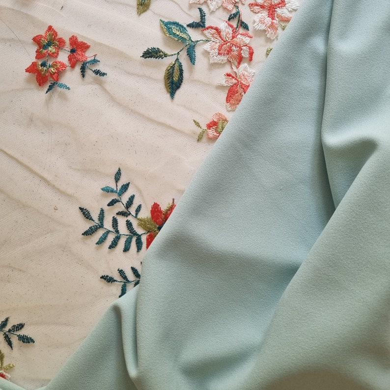 Pu&ograve; includere: Un tessuto blu chiaro con un delicato ricamo floreale in tonalit&agrave; di rosso, verde e bianco.