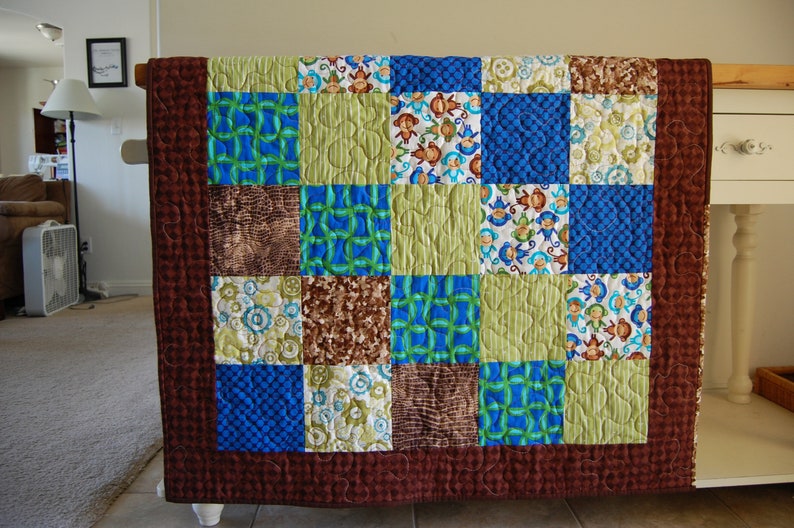 May include: A brown, green and blue patchwork quilt with a quilted pattern. The quilt is made up of 16 squares, each with a different pattern. The quilt is hanging on a wall.