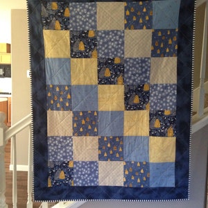 May include: A blue and yellow patchwork quilt with a white border. The quilt is made of squares of different fabrics, each with a different pattern. The quilt is hanging on a wall.
