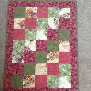 May include: A patchwork quilt with a green and red colour scheme. The quilt is made of squares with a floral pattern.