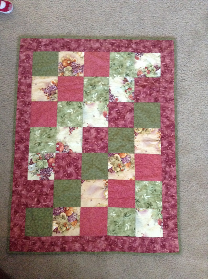 May include: A patchwork quilt with a green and red colour scheme. The quilt is made of squares with a floral pattern.