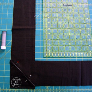 May include: A close-up of a black fabric corner being sewn with pins and a ruler. The fabric is on a green cutting mat. The text "Made By Jaime" is visible in the bottom left corner.