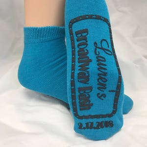 May include: A pair of blue ankle socks with a black printed design on the bottom. The design includes the text "Lauren's Bridal Day" and the date "2.17.2018".