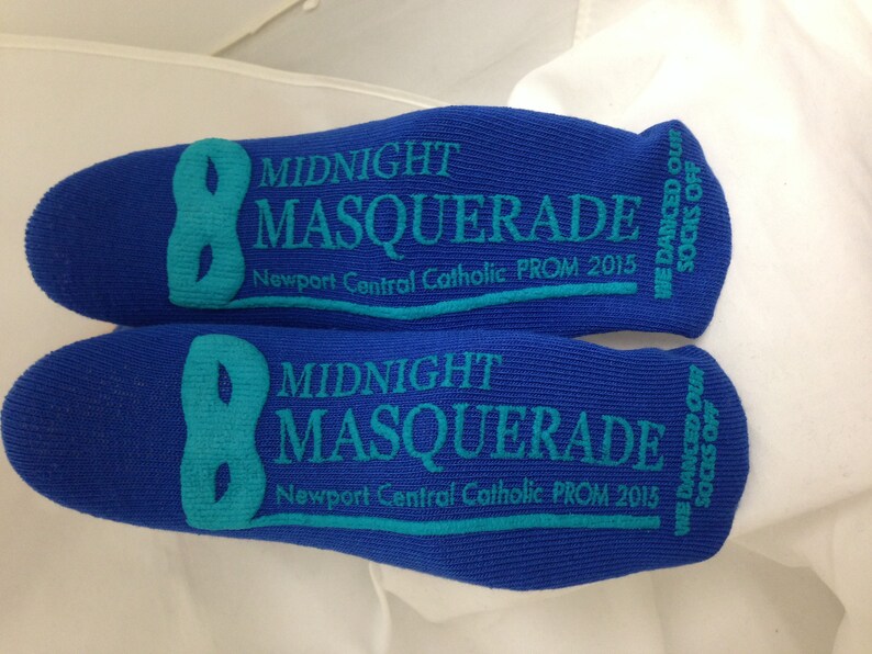 May include: A pair of blue socks with the text "Midnight Masquerade" and "Newport Central Catholic PROM 2015" printed on them. The socks also have a teal mask design and the text "We danced our socks off".