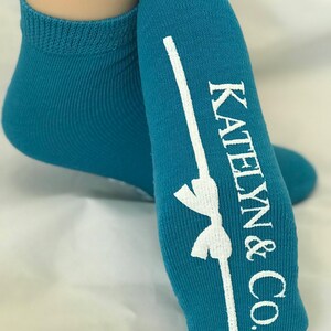 May include: Teal blue ankle socks with a white bow and the text "Katelyn & Co." printed on the heel.